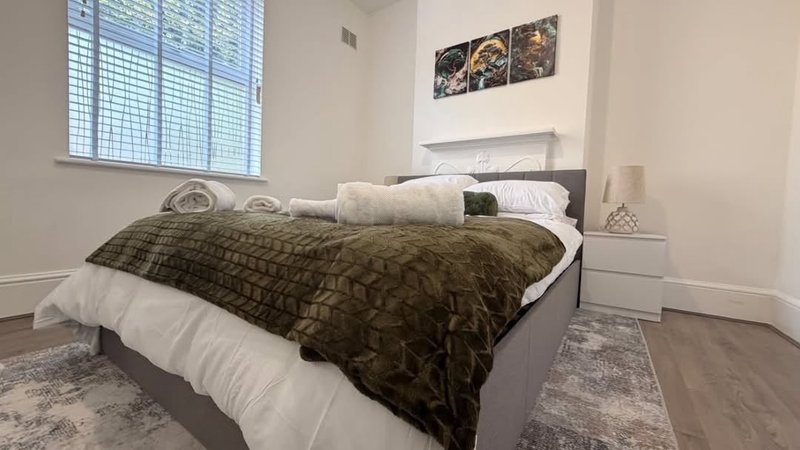 Modern bedroom with double bed, olive green bedding, white pillows and contemporary wall art