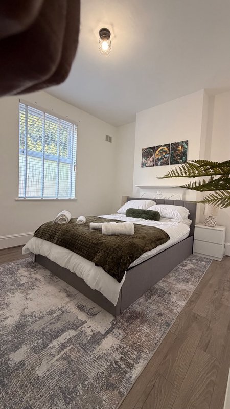 Modern bedroom with grey upholstered bed, white bedding, olive throw, potted plant and window