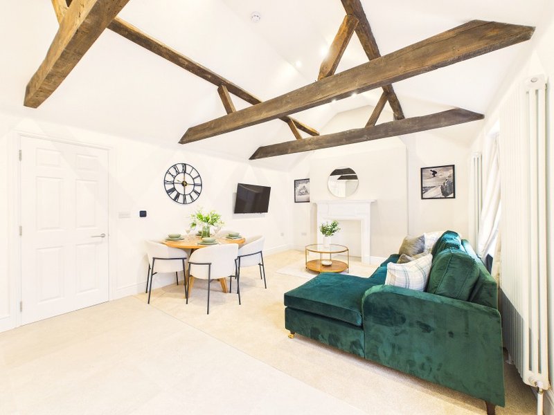 Open-plan living room with exposed wooden beams, green velvet sofa, dining table and white walls