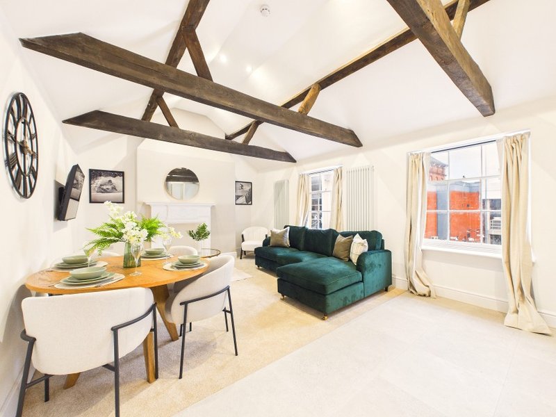 Open-plan living space with exposed beams, dining table, green sofa and glass doors
