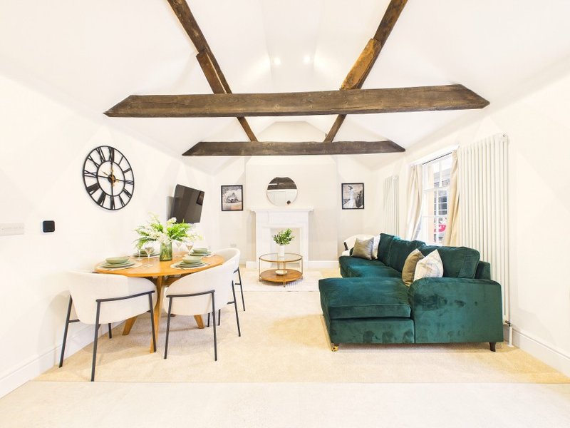 Open-plan living space with exposed wooden beams, dining table, green sofa, and clock on wall