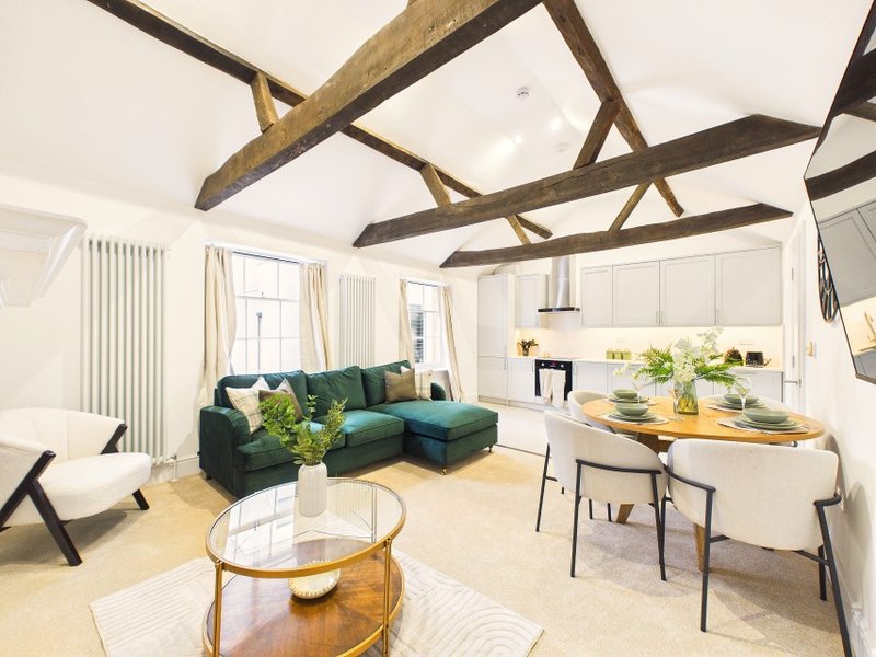 Open-plan living space with exposed wooden beams, green sectional sofa, dining table and kitchen area
