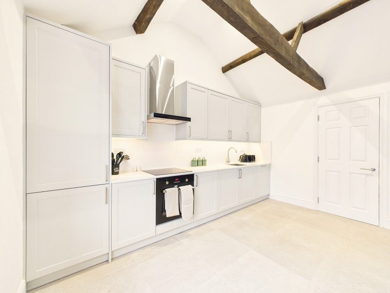 Modern kitchen with white cabinetry, black oven, exposed wooden beams, and light flooring