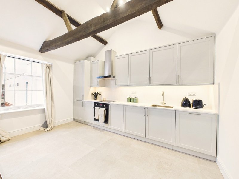 Modern kitchen with white cabinetry, exposed beam ceiling, and window overlooking street