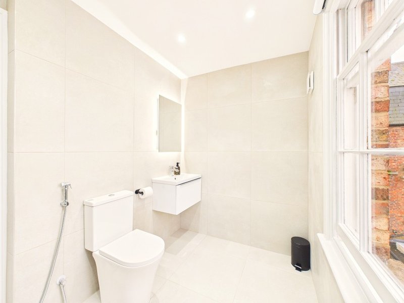 Modern bathroom with white tiles, toilet, sink, mirror and window