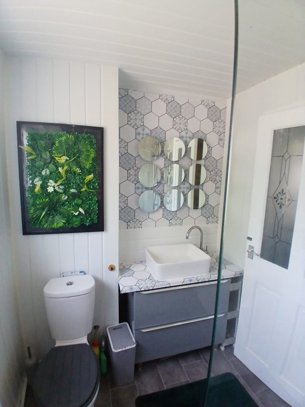 Modern bathroom with toilet, vanity with dark drawers, walk-in shower with geometric tile pattern and wall art
