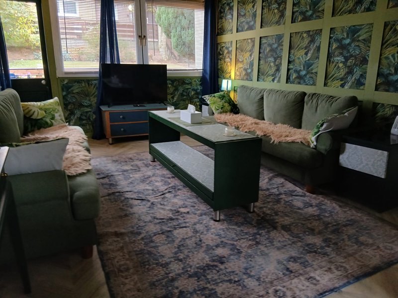 Living room with green sofas, black coffee table, TV, and botanical wall art