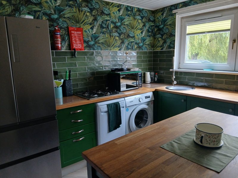 Modern kitchen with green cabinetry, wood countertops, washing machine and green tile backsplash