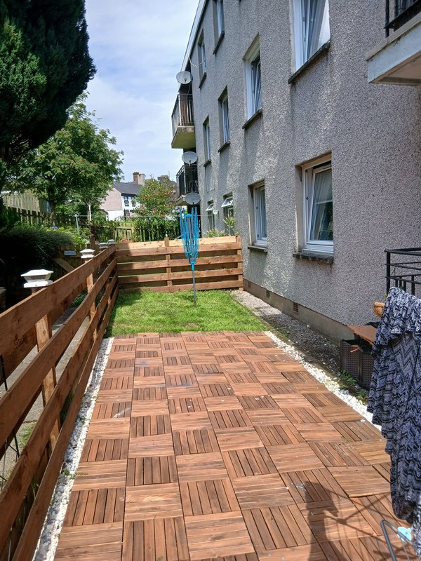 Residential garden with wooden deck, raised beds, and multi-story apartment building