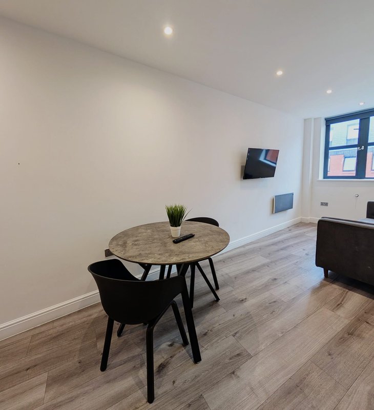 Modern studio apartment with round dining table, black chair, wall-mounted TV, and wood flooring