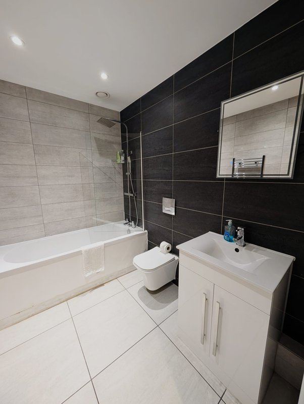 Modern bathroom with white vanity, black tile walls, bathtub and toilet