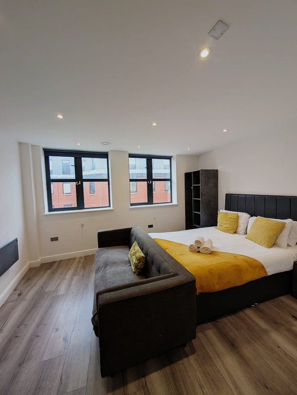 Modern bedroom with black bed, yellow bedding, windows, black shelving unit and wooden flooring