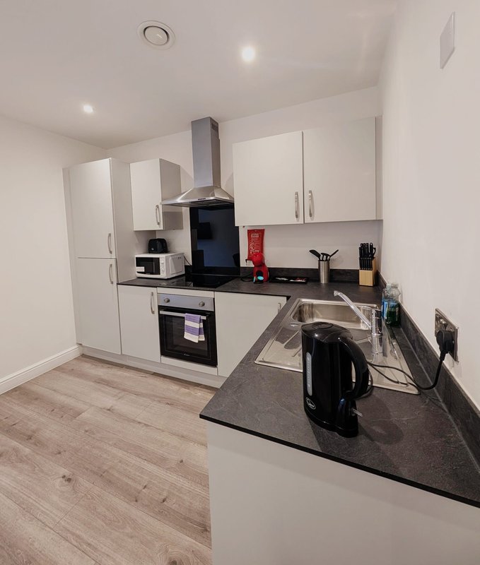 Modern white kitchen with black countertop, integrated appliances, and wooden flooring