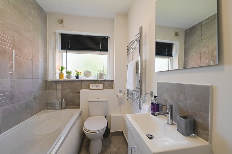 Modern bathroom with bathtub, toilet, sink, mirror and tiled walls