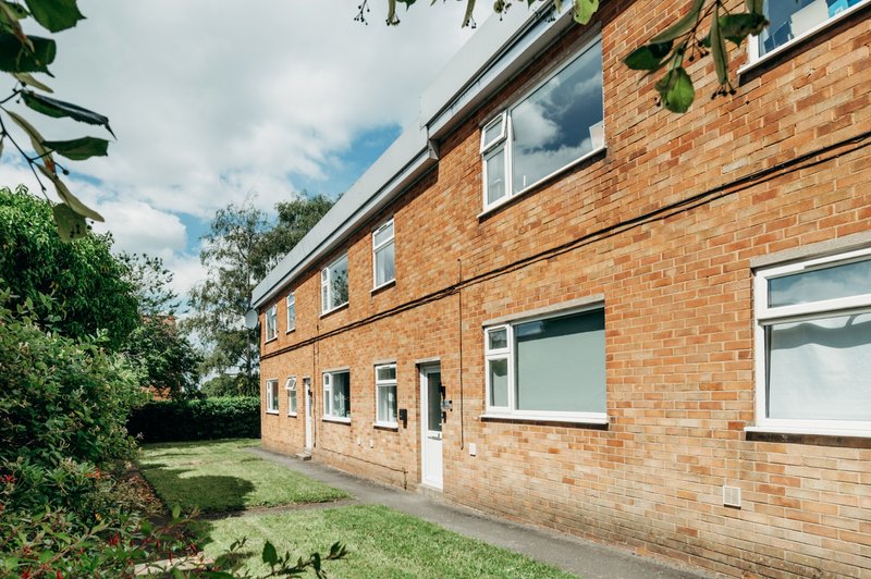 Brick residential building exterior with windows, garden, and green landscaping