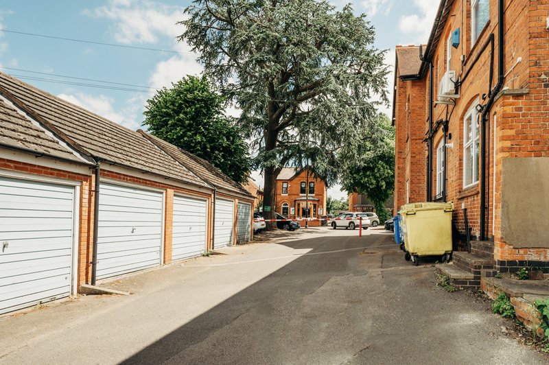 Brick cottage with white garage doors, driveway, mature tree and parked vehicles