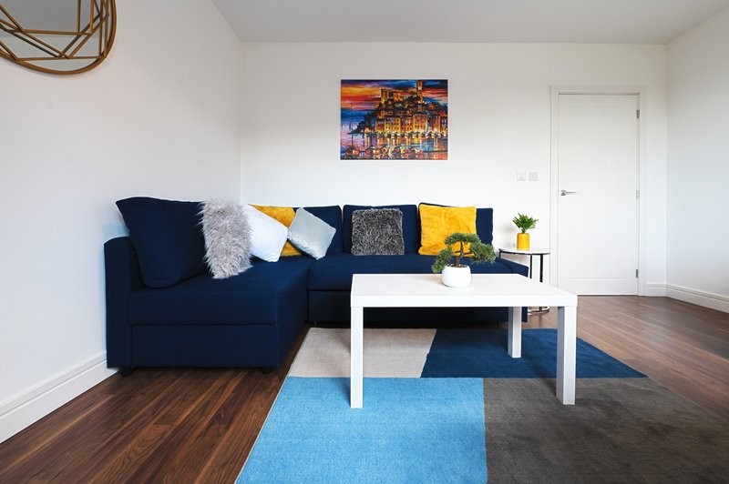 Living room with navy corner sofa, white coffee table, geometric rug and framed cityscape art