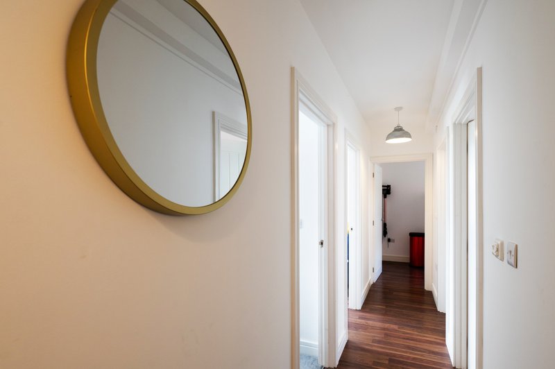 Bright hallway with round mirror, white doors, wooden flooring and pendant lighting