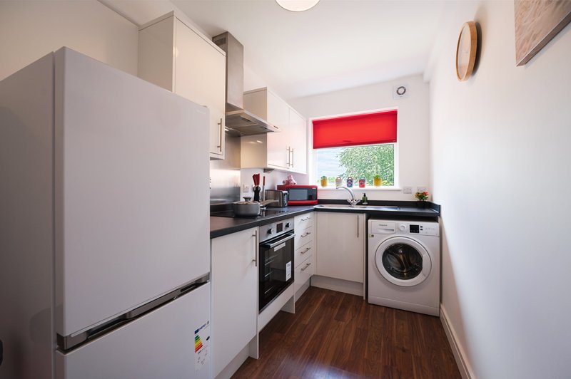 Modern kitchen with white cabinetry, stainless steel appliances, washing machine and wooden flooring