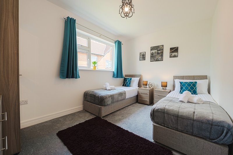 Bright twin bedroom with two single beds, teal curtains, wooden door and pendant light