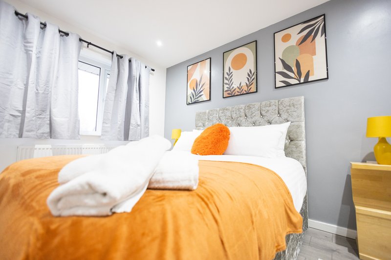 Bright bedroom with double bed, orange bedding, grey headboard and framed botanical wall art