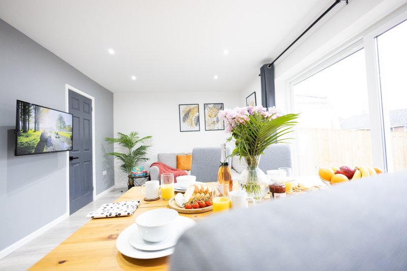 Modern kitchen and living area with wooden counter, fresh flowers, fruit bowl, and bright windows