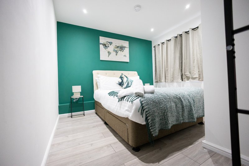 Modern bedroom with teal accent wall, double bed, grey bedding, and light wood flooring