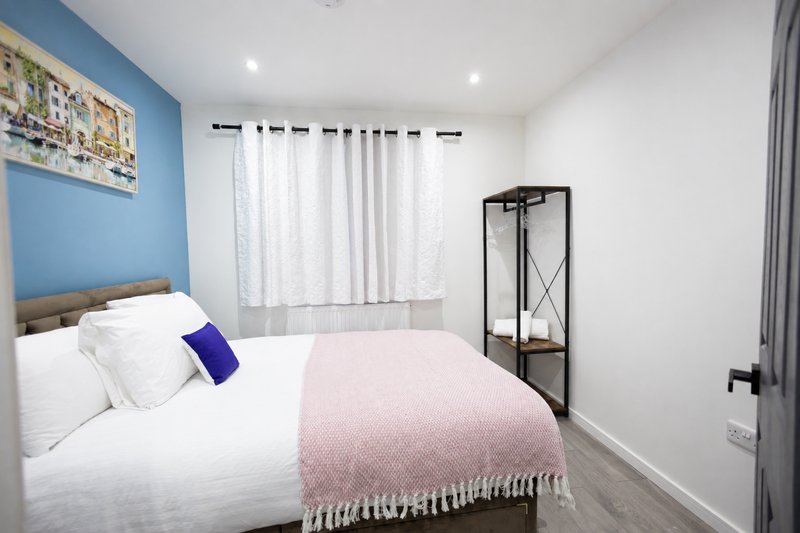 Bright bedroom with double bed, blue accent wall, white curtains and modern furnishings