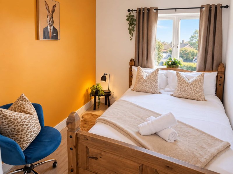 Bright bedroom with double bed, wooden frame, patterned cushions, blue chair, and large window with garden view