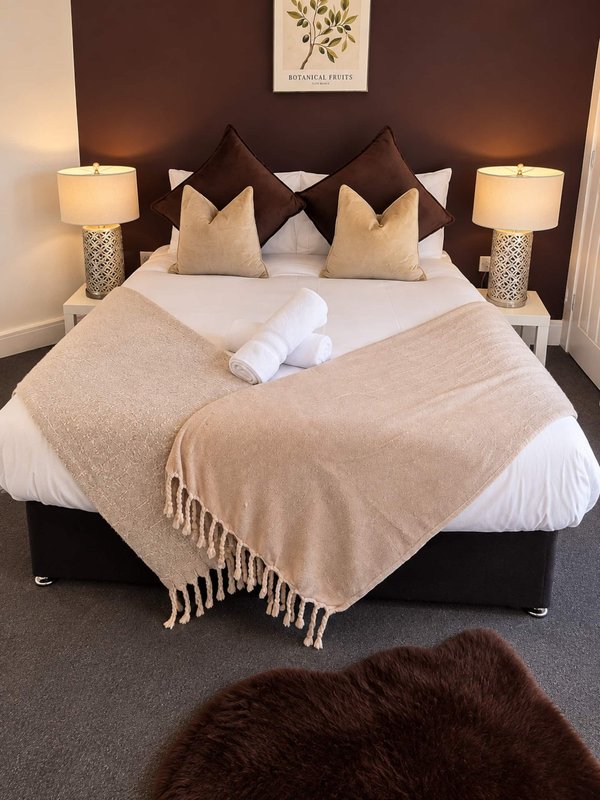 Modern bedroom with queen bed, brown headboard, decorative pillows, throw blanket and bedside lamps