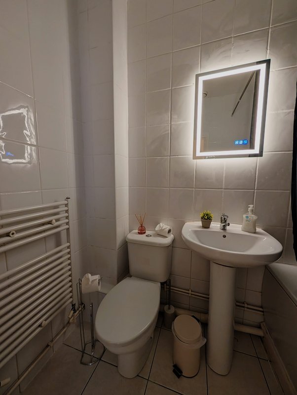 Modern bathroom with illuminated mirror, pedestal sink, toilet, heated towel rail and tiled walls