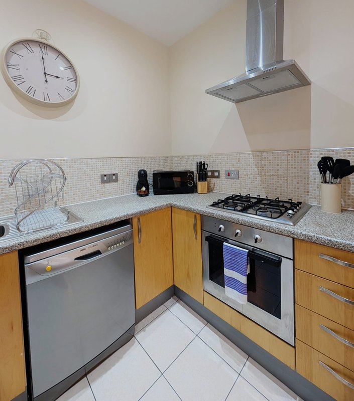 Modern kitchen with wooden cabinets, stainless steel appliances, gas hob, and wall clock
