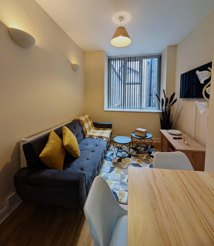 Modern living room with black sofa, yellow cushions, wooden desk, blue rug and vertical blinds