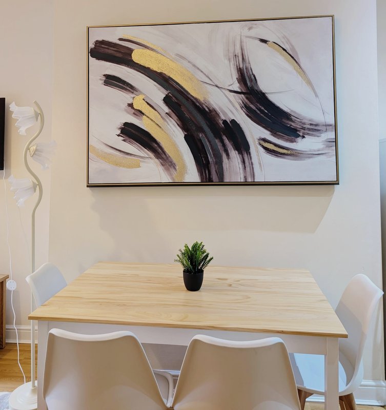 Dining area with wooden table, white chairs, abstract wall art, and potted plant