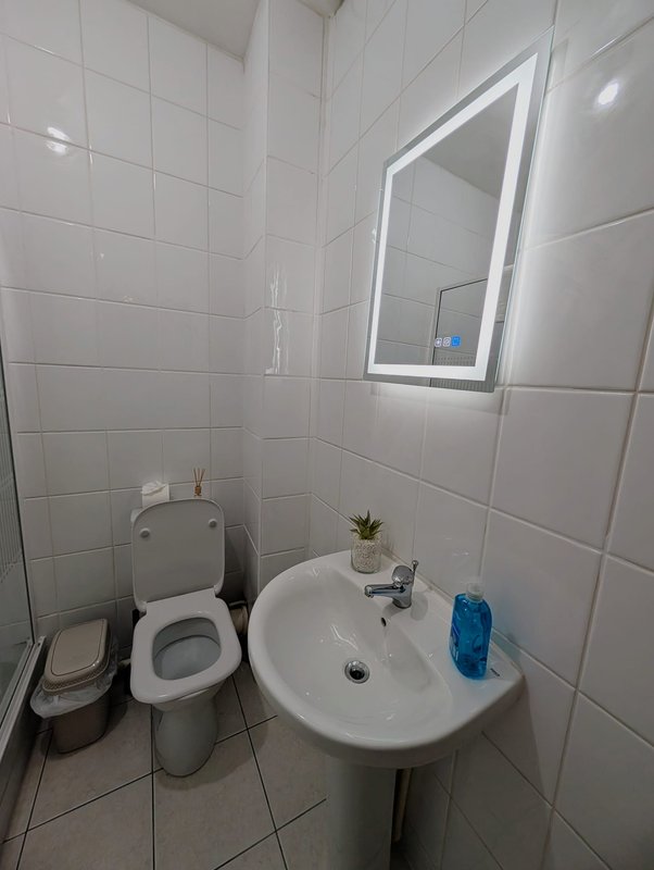Clean white bathroom with toilet, pedestal sink, illuminated mirror and tiled walls