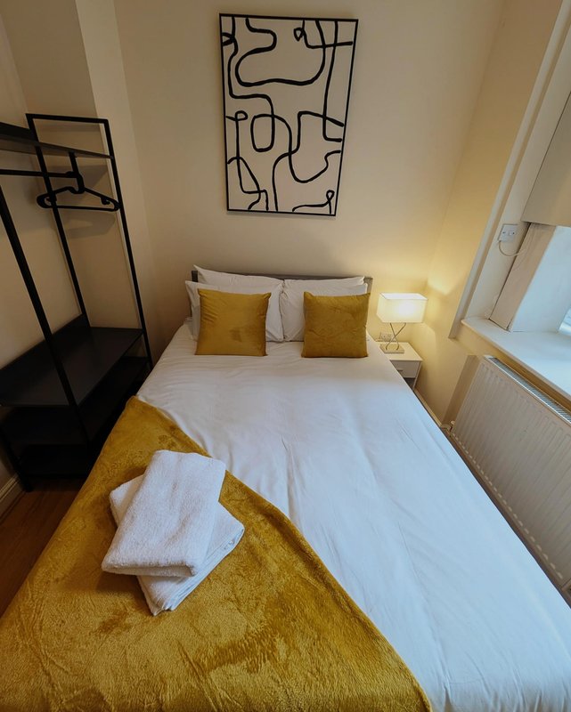 Bedroom with double bed, yellow bedding, white pillows, wall art and bedside lamp