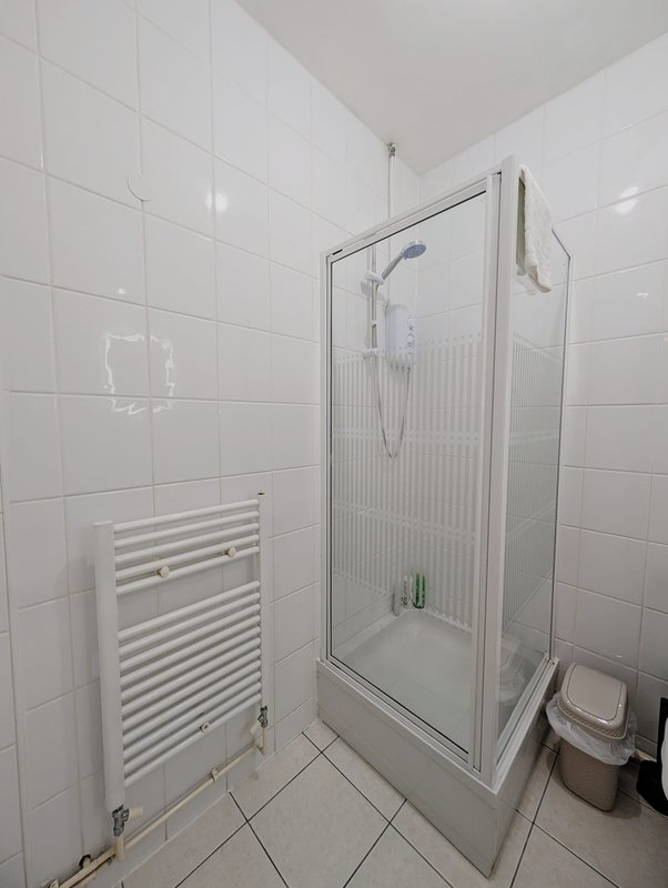 Clean white-tiled bathroom with shower enclosure, heated towel rail, and toilet
