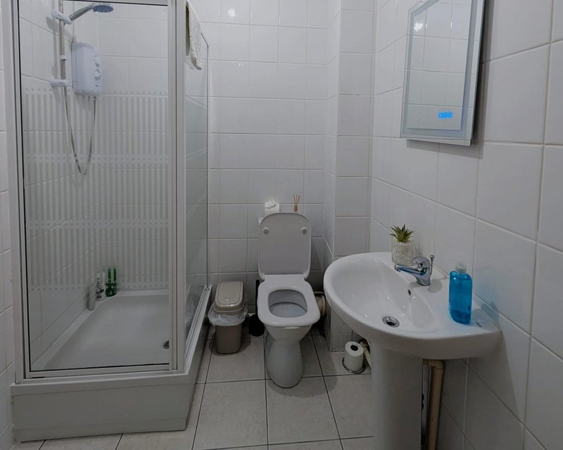 Clean bathroom with shower cubicle, toilet, sink and white tile walls
