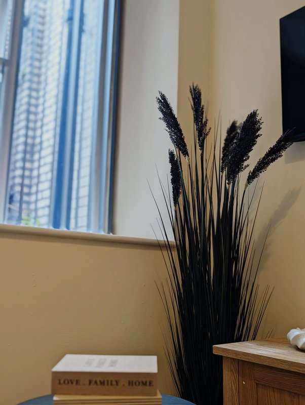 Yellow bedroom wall with decorative black pampas grass, wooden furniture, and window view