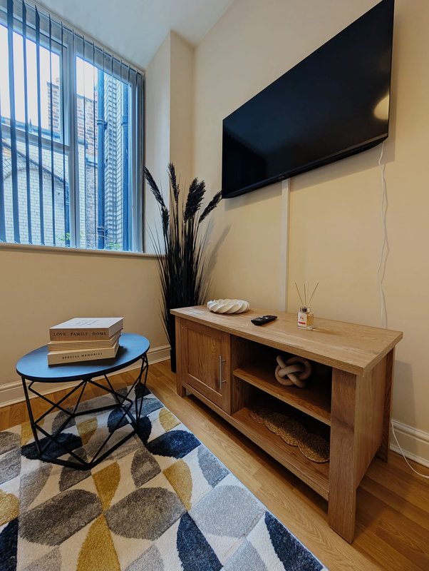 Modern bedroom with wall-mounted TV, wooden media console, small blue side table and geometric area rug