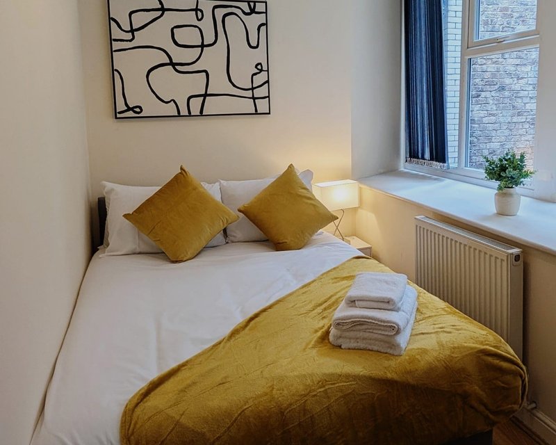 Bright bedroom with double bed, yellow bedding, pillows, and framed abstract wall art