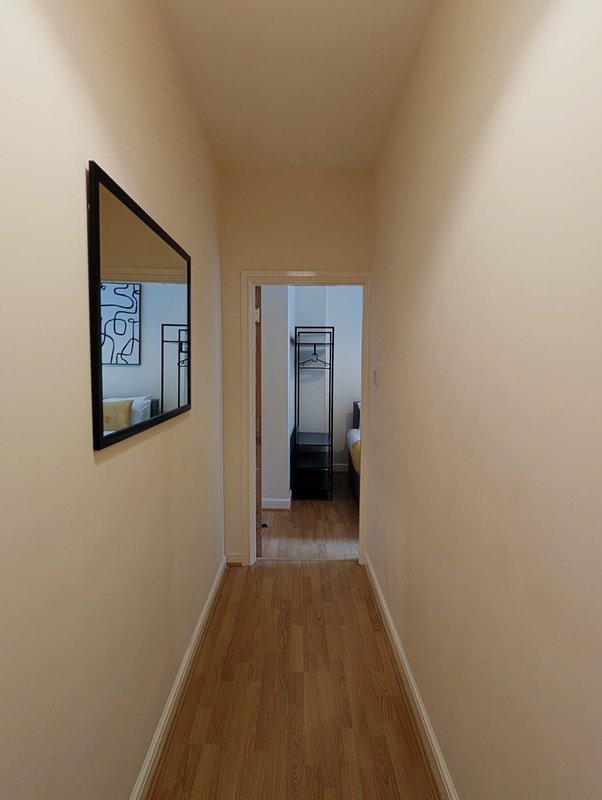 Narrow hallway with wooden flooring, beige walls, framed artwork and doorway