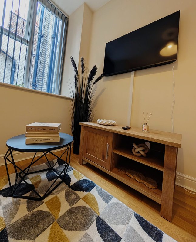 Living room with wall-mounted TV, wooden media console, round blue table, and geometric patterned rug