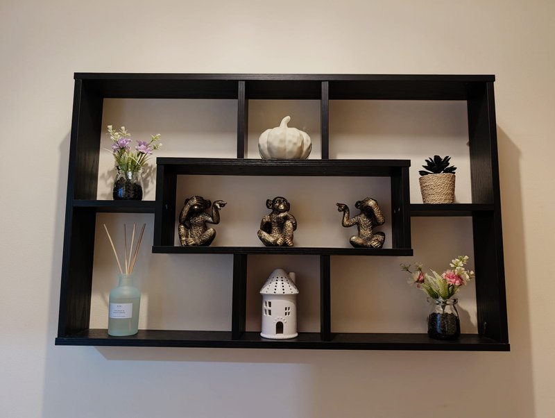 Black wall-mounted shelving unit displaying decorative items including flowers, vases, sculptures and ornaments