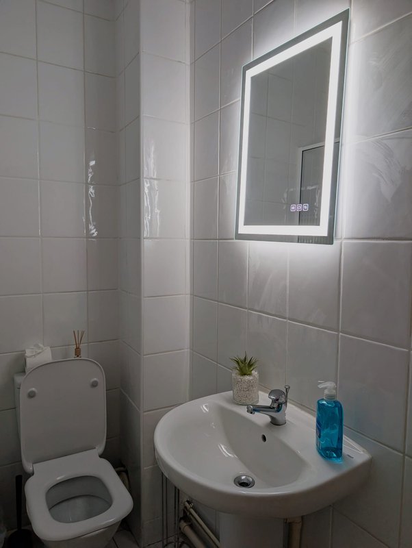 Modern bathroom with white tiles, round sink, illuminated mirror and toilet