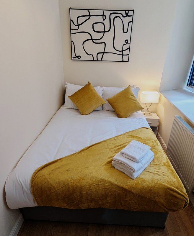 Bright bedroom with double bed, mustard-yellow bedding, decorative cushions and abstract wall art