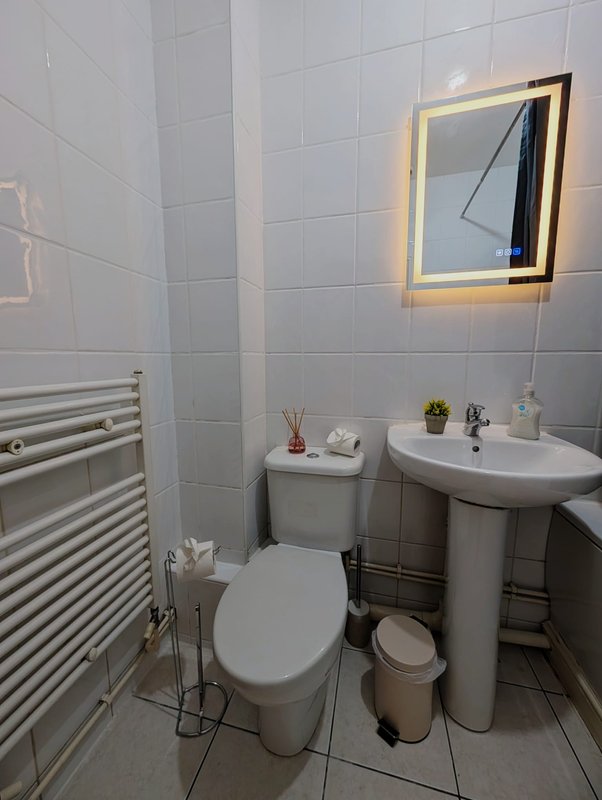 Modern bathroom with toilet, pedestal sink, illuminated mirror and heated towel rail