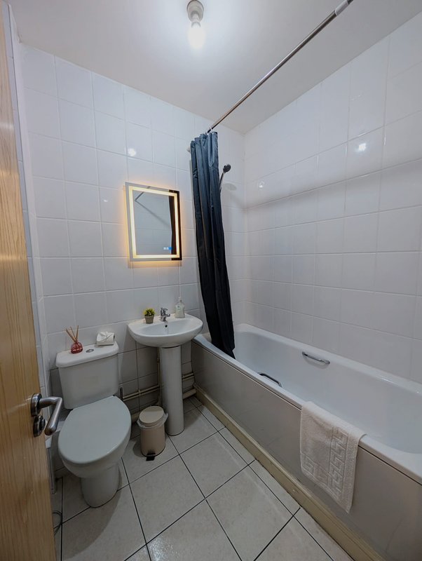 Clean modern bathroom with toilet, pedestal sink, bathtub and illuminated mirror