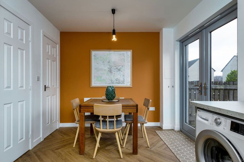 Dining area with wooden table, chairs, orange accent wall, and washing machine visible