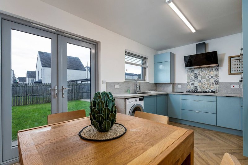 Modern kitchen with blue cabinetry, wooden island, and garden view through patio doors